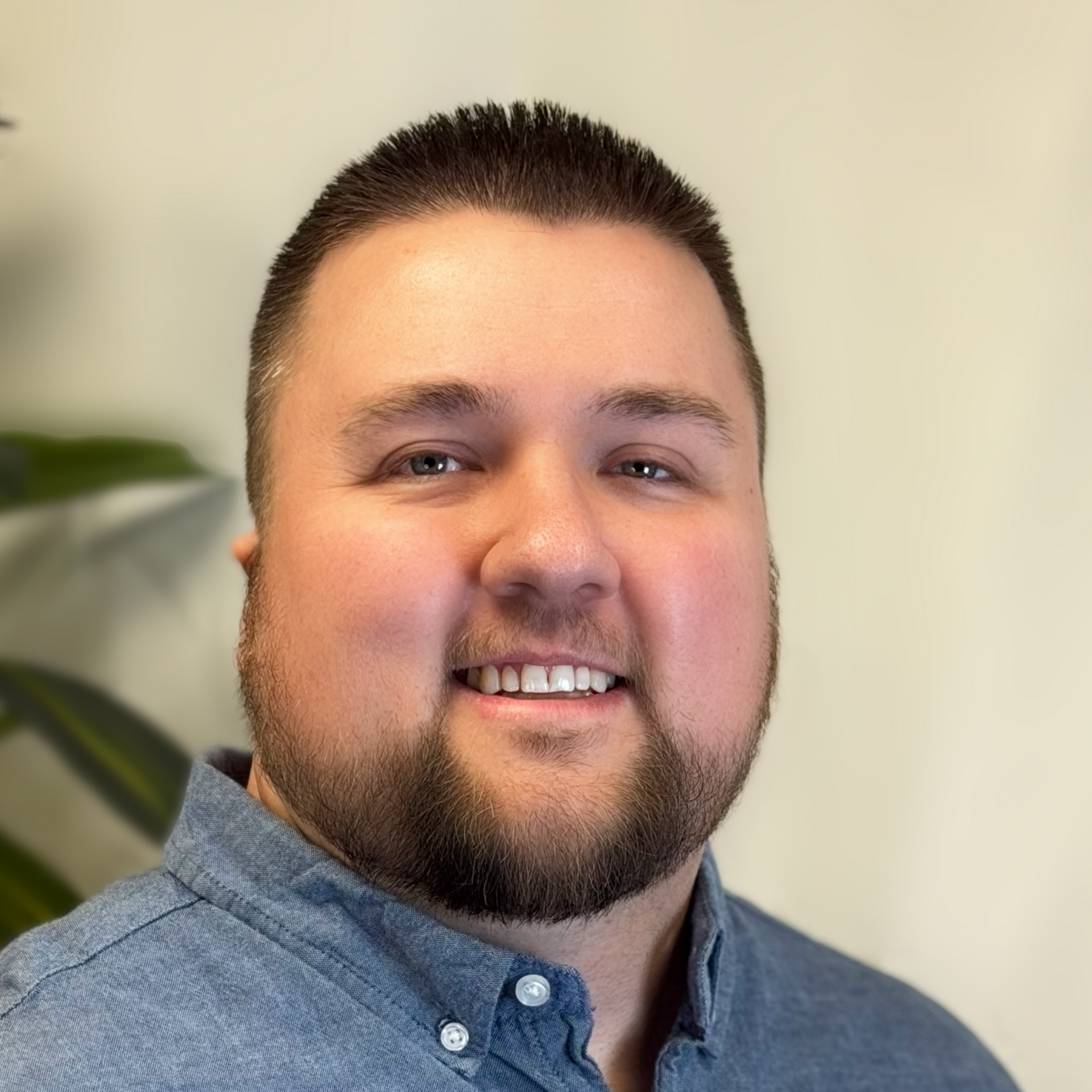 Man with short brown hair and beard, smiling, wearing a blue button-down shirt.
