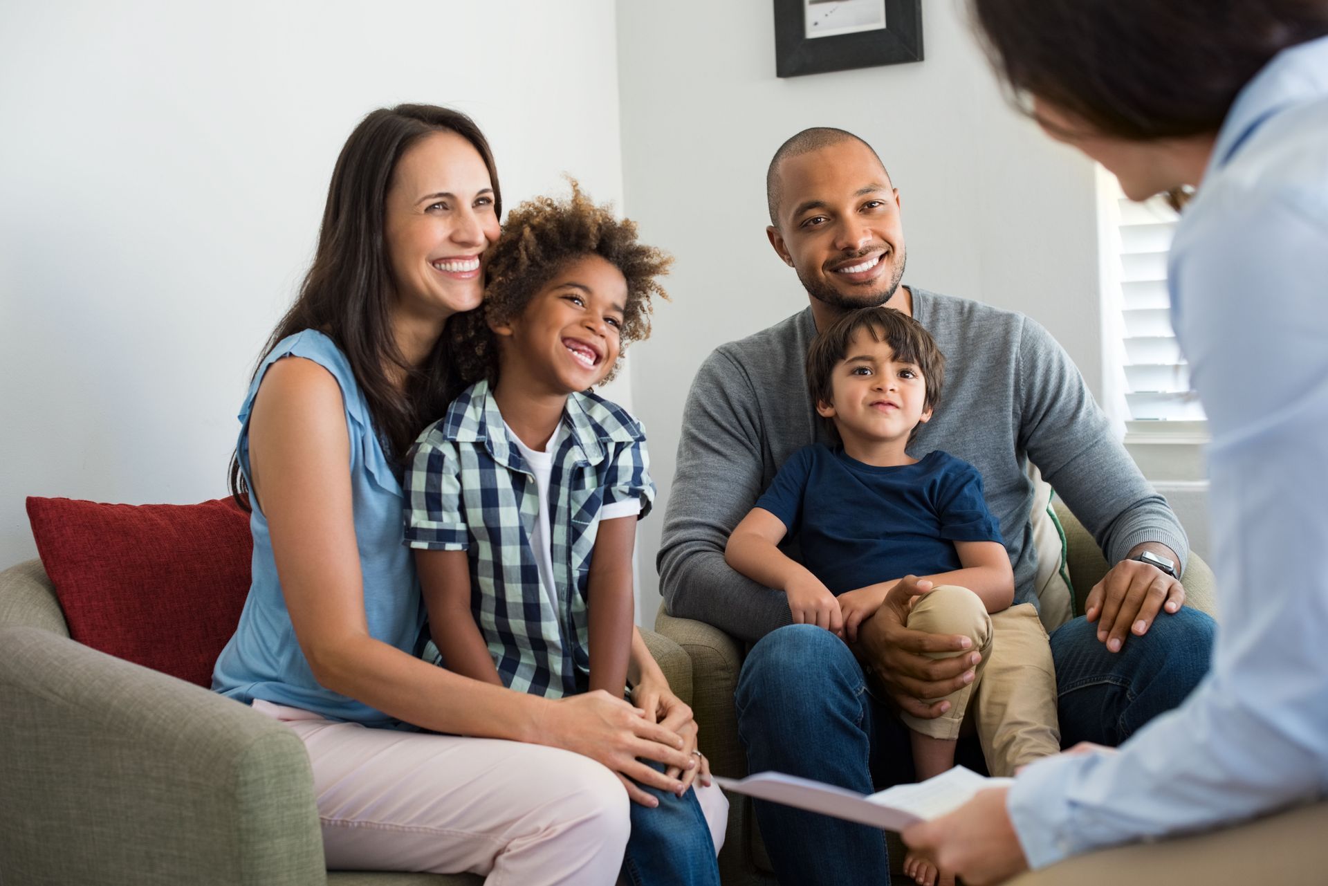 Family of four smiling, sitting in a therapist's office. Parents and children seated together, looking at the therapist.