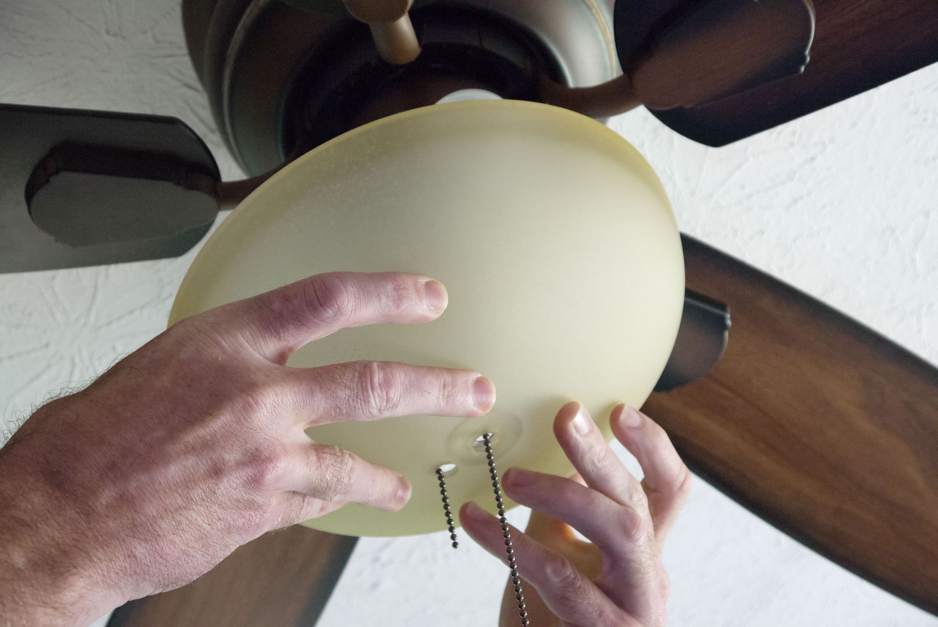Hands installing a light globe onto a ceiling fan.