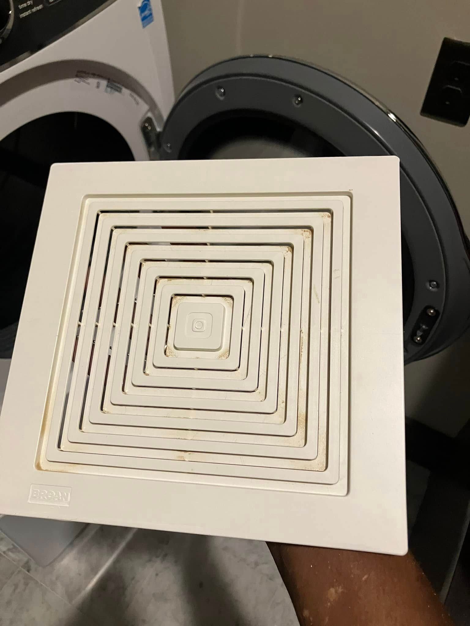 A person is holding a ventilation fan in front of a washing machine.