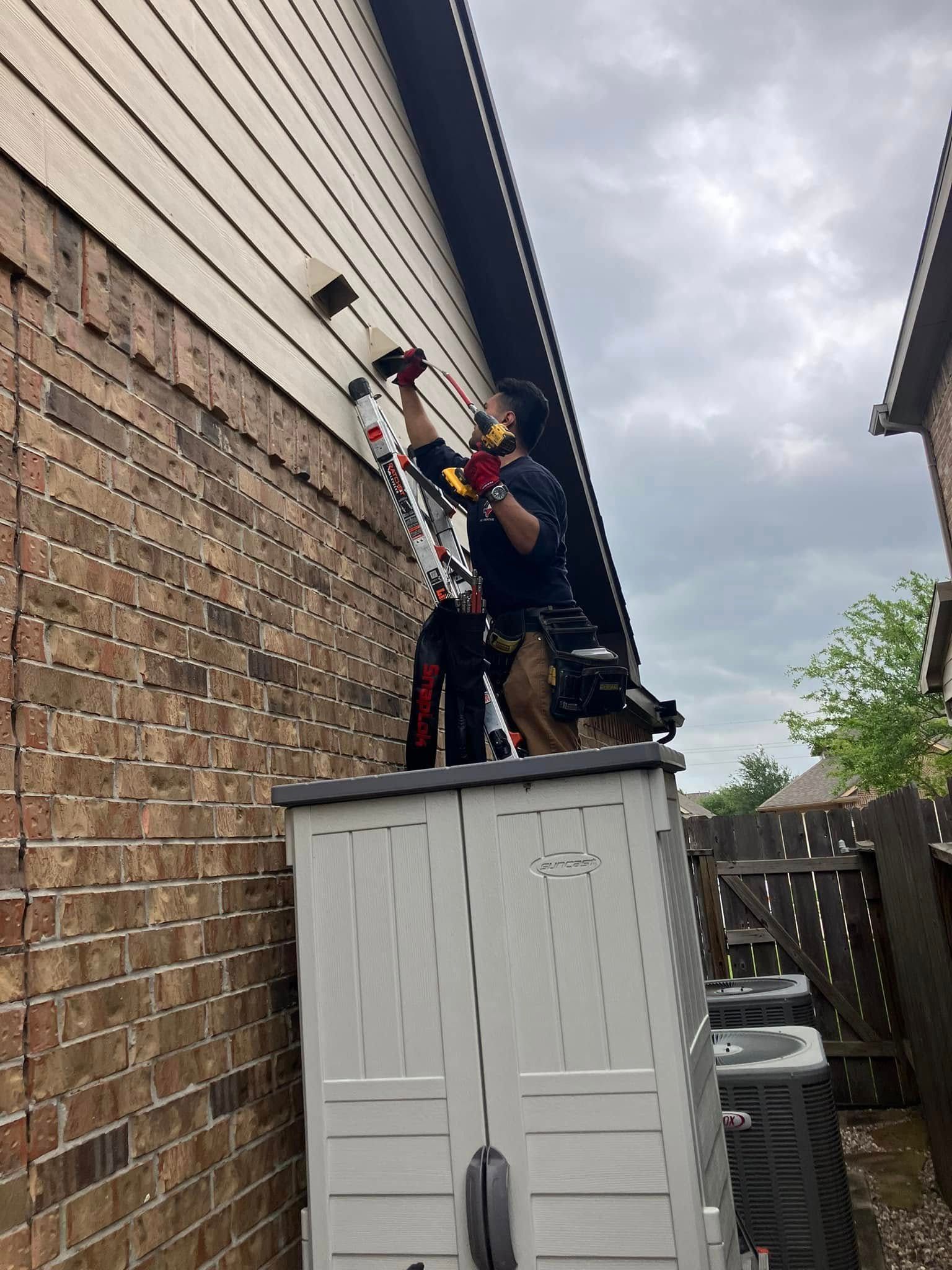 A man is installing a security camera on the side of a house.