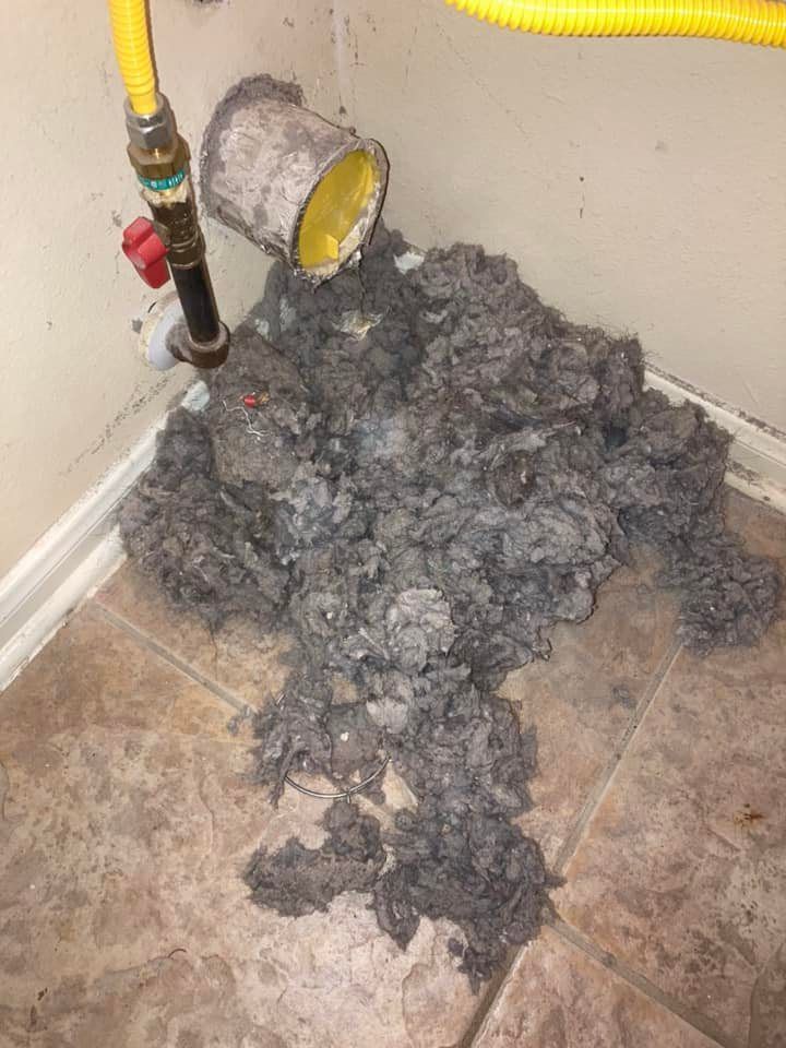 A pile of lint is sitting on the floor next to a pipe.