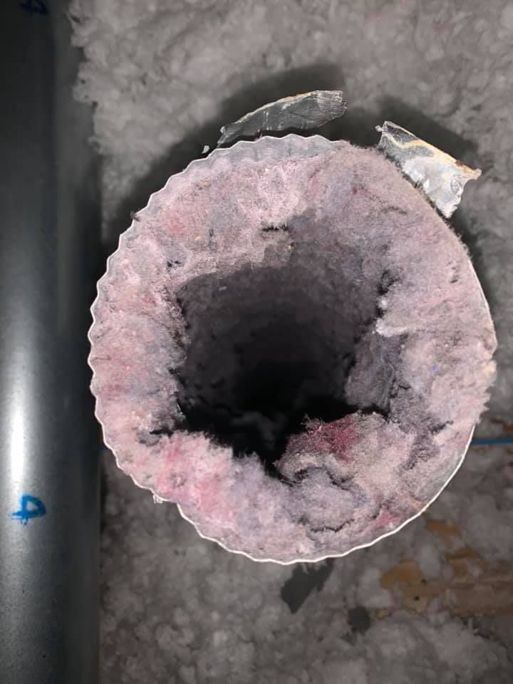 A close up of a dirty duct with a hole in it.