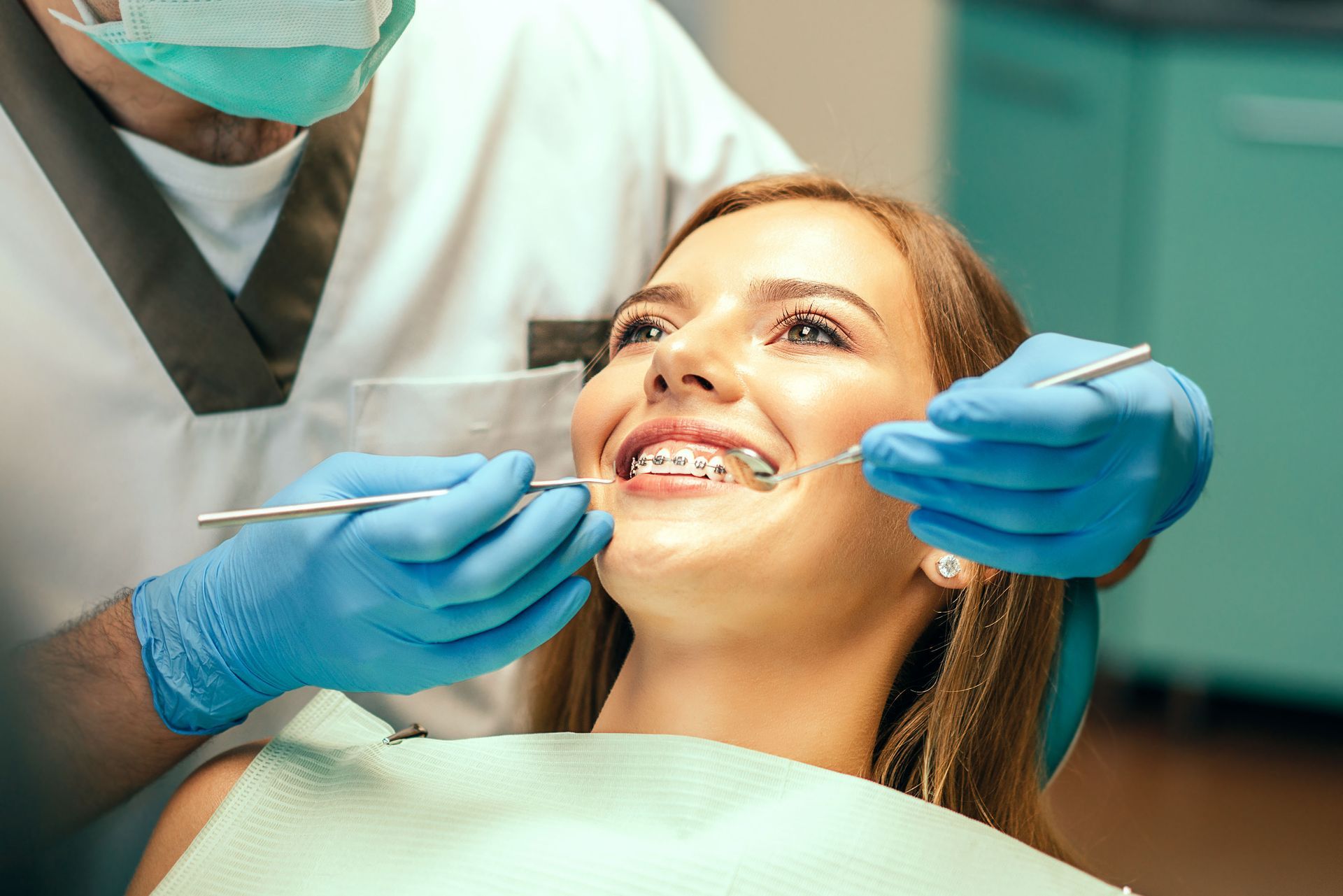 Dentist examining a patient's braces. Patient smiles while dentist holds tools, blue gloves visible.