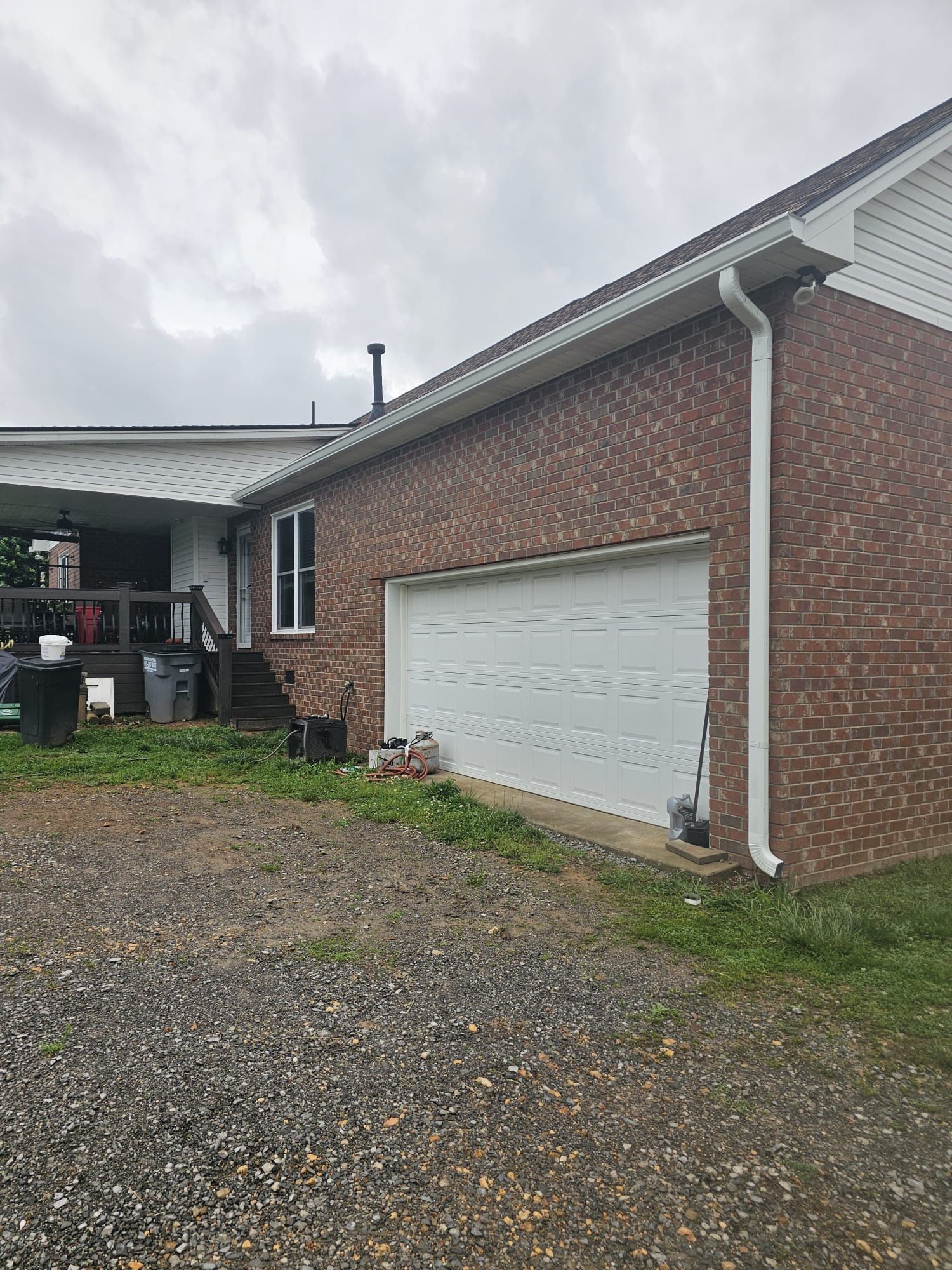 A brick house with a white garage door, white trim, and a gravel driveway under a cloudy sky.