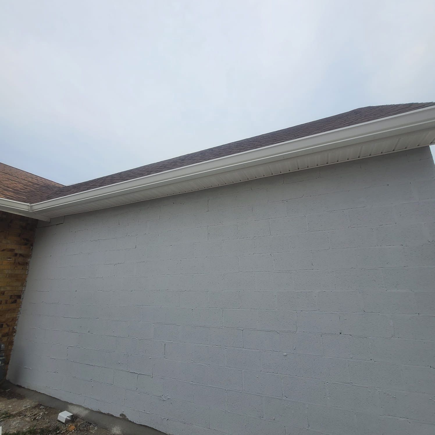 An exterior view of a grey concrete block wall beneath a sloped, tiled roof with white trim and gutters against a sky.