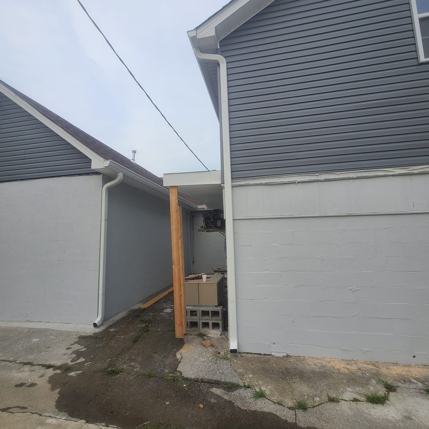 A narrow alley between two gray buildings with gray siding, featuring a small covered area supported by a wooden post.