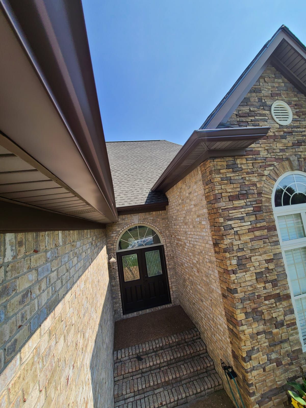 A ground-level view of a house entrance with stone siding, a dark front door, and a tiled walkway under a clear blue sky.