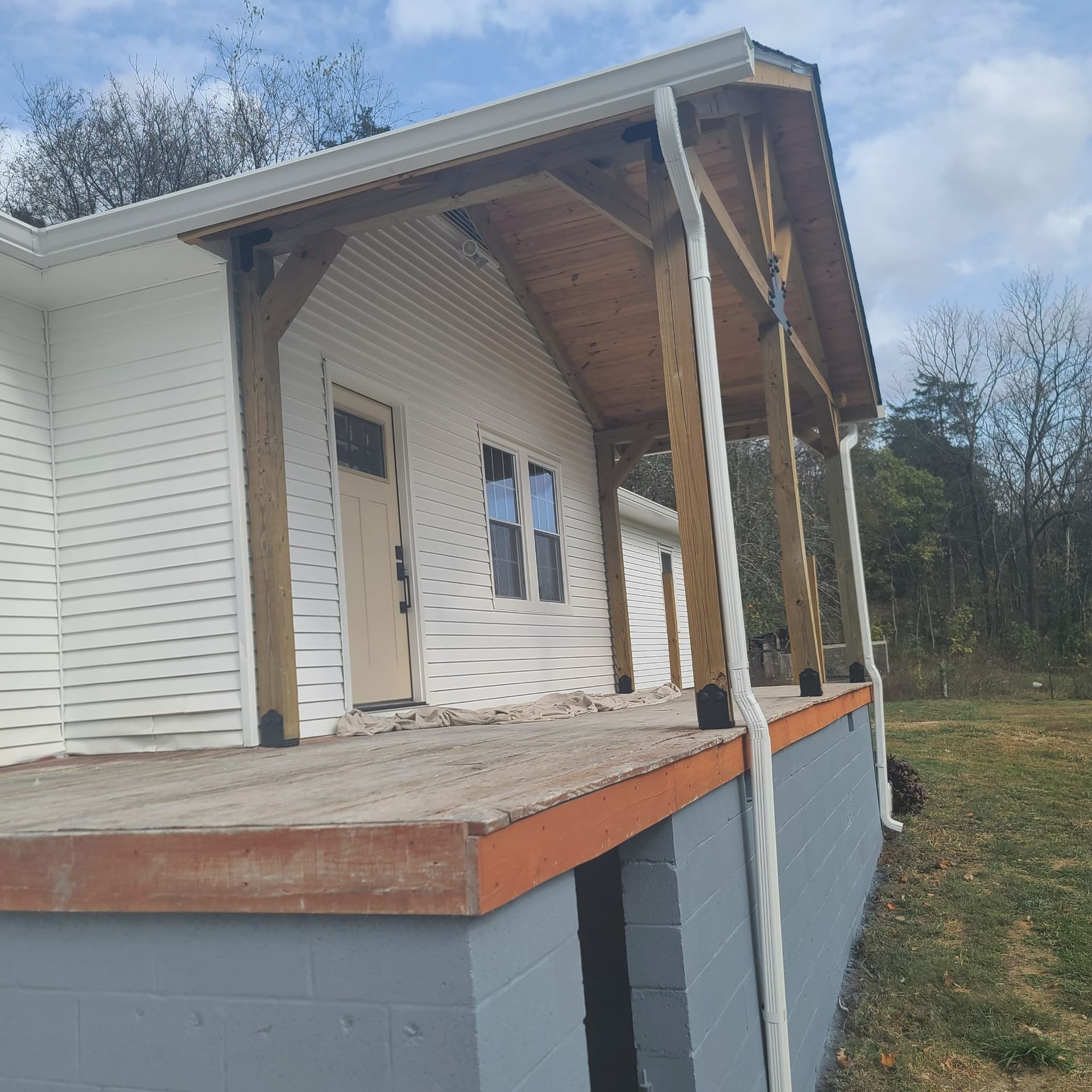 A white house with a partially constructed wooden front porch, featuring timber support beams and a gray block foundation.