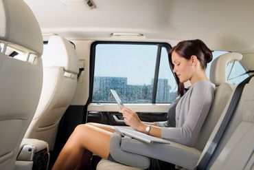 Woman works on a tablet in the backseat of a car. She has her legs stretched out.