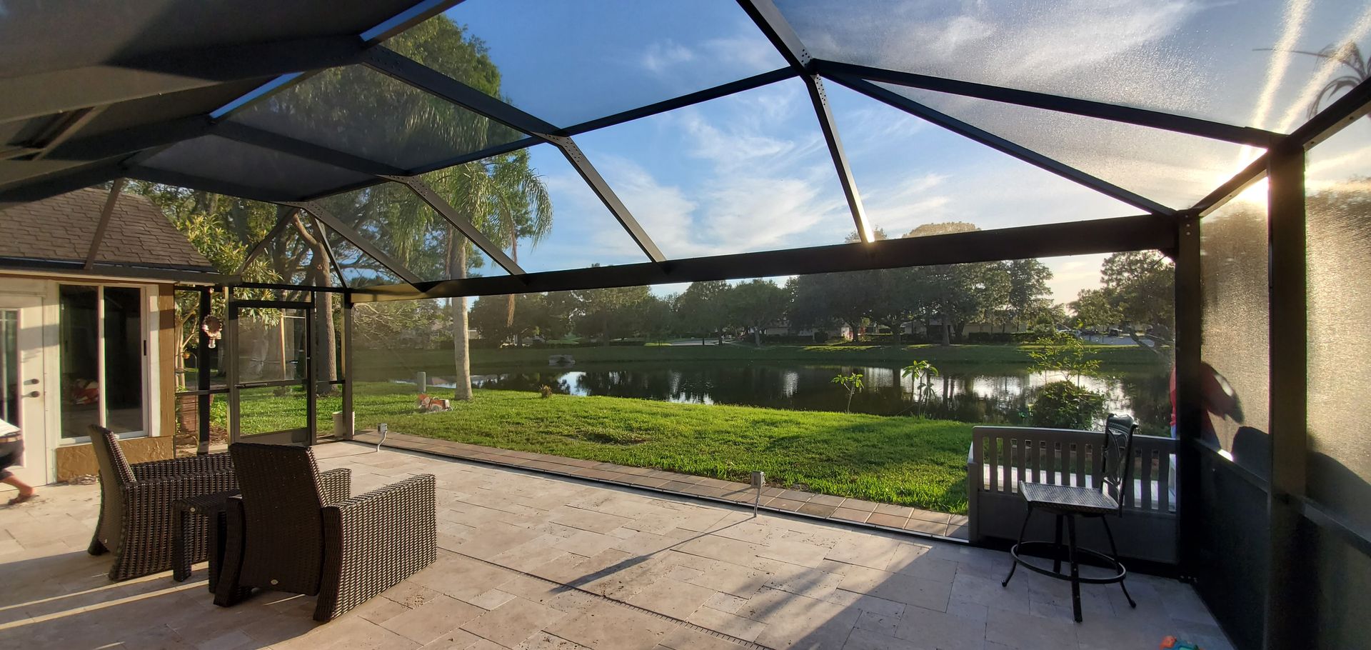 Covered patio with chairs, overlooking a sunny lawn and lake through a screened enclosure