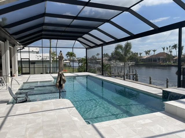 Screened backyard pool with turquoise water, lounge chairs, and a waterfront view under a covered patio