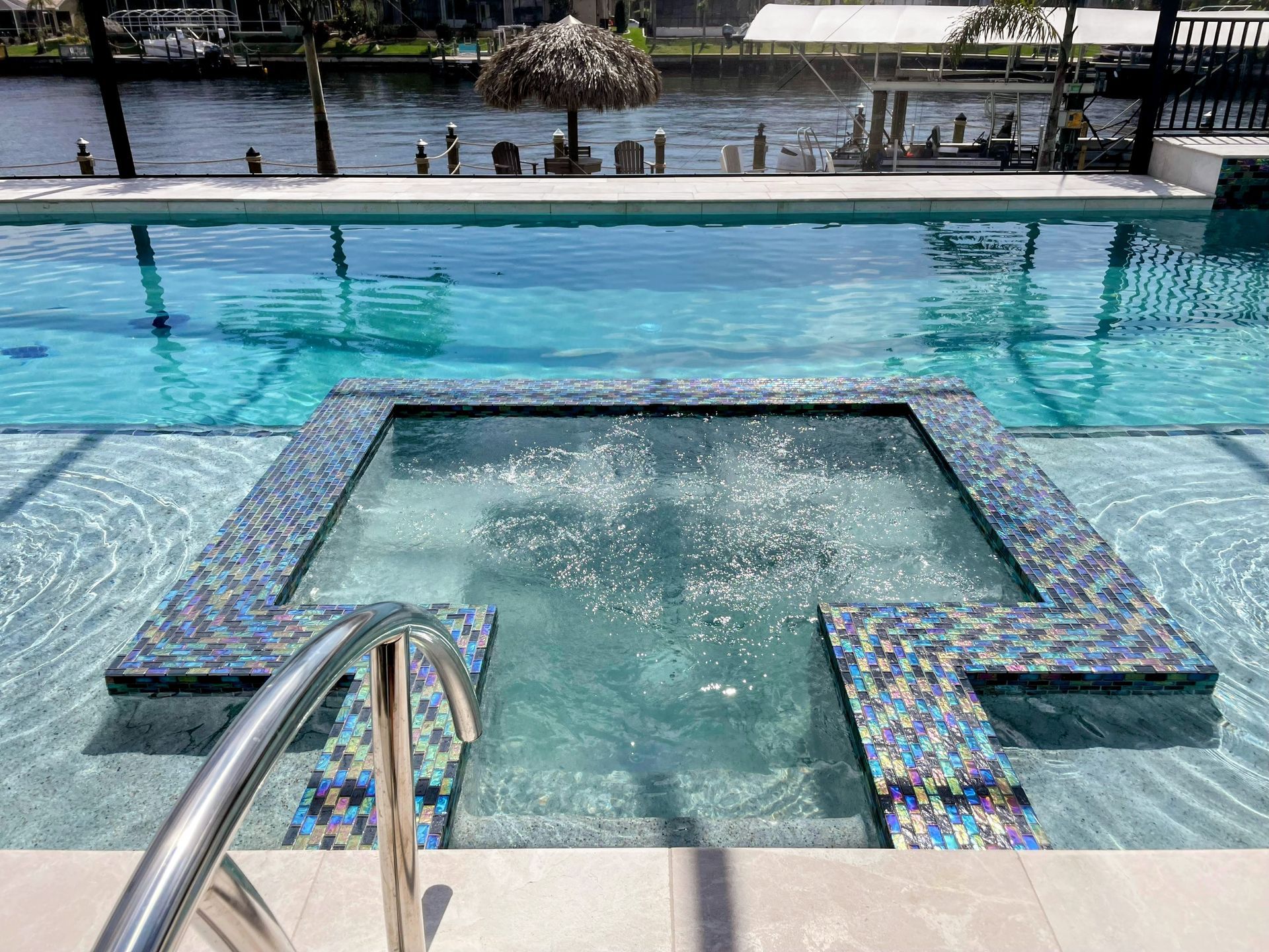 Pool with a tiled submerged platform and metal handrail leading into turquoise water