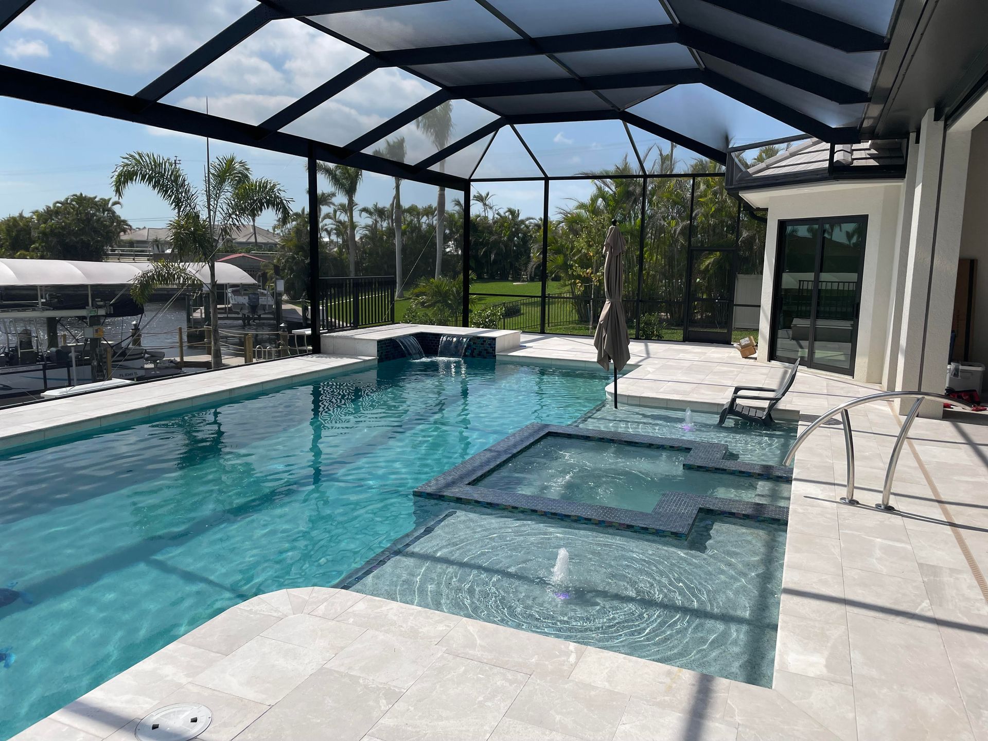 Screened backyard pool with sun shelf, blue water, and patio lounge chairs under a metal enclosure