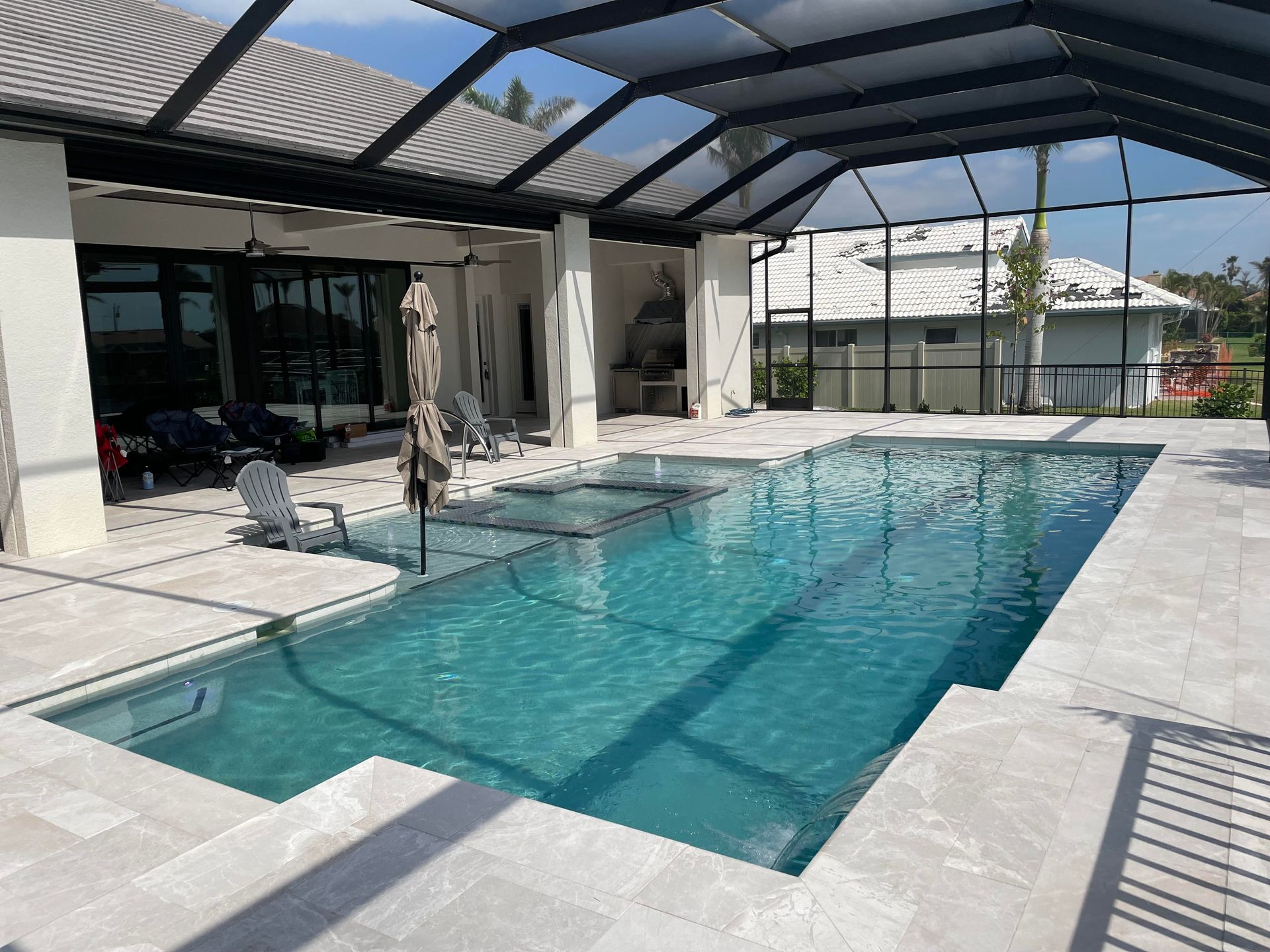 Outdoor patio with a rectangular turquoise swimming pool under a covered lanai, beside a modern house.