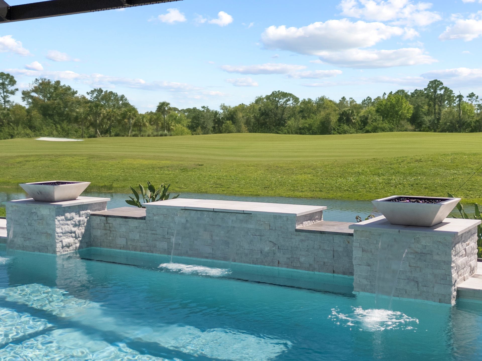 Backyard pool with stone waterfall edge overlooking a green golf course under a blue sky