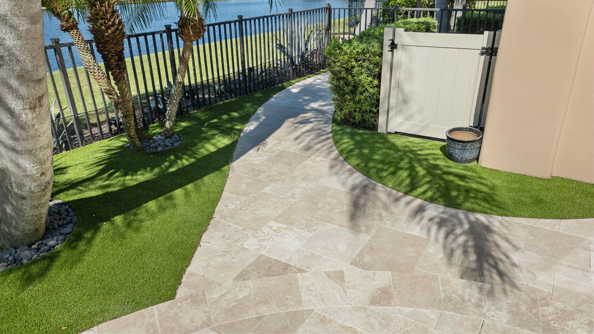 Stone patio path beside green lawn, fence, and tan building near the water