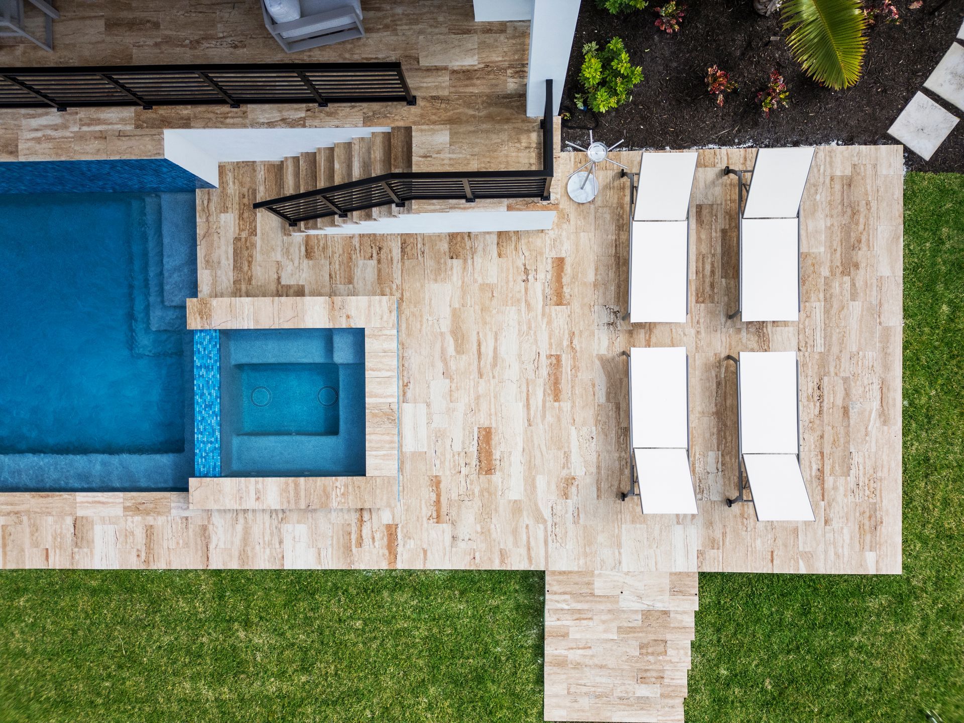 Aerial view of a backyard patio with a blue pool, lounge chairs, and a small lawn.