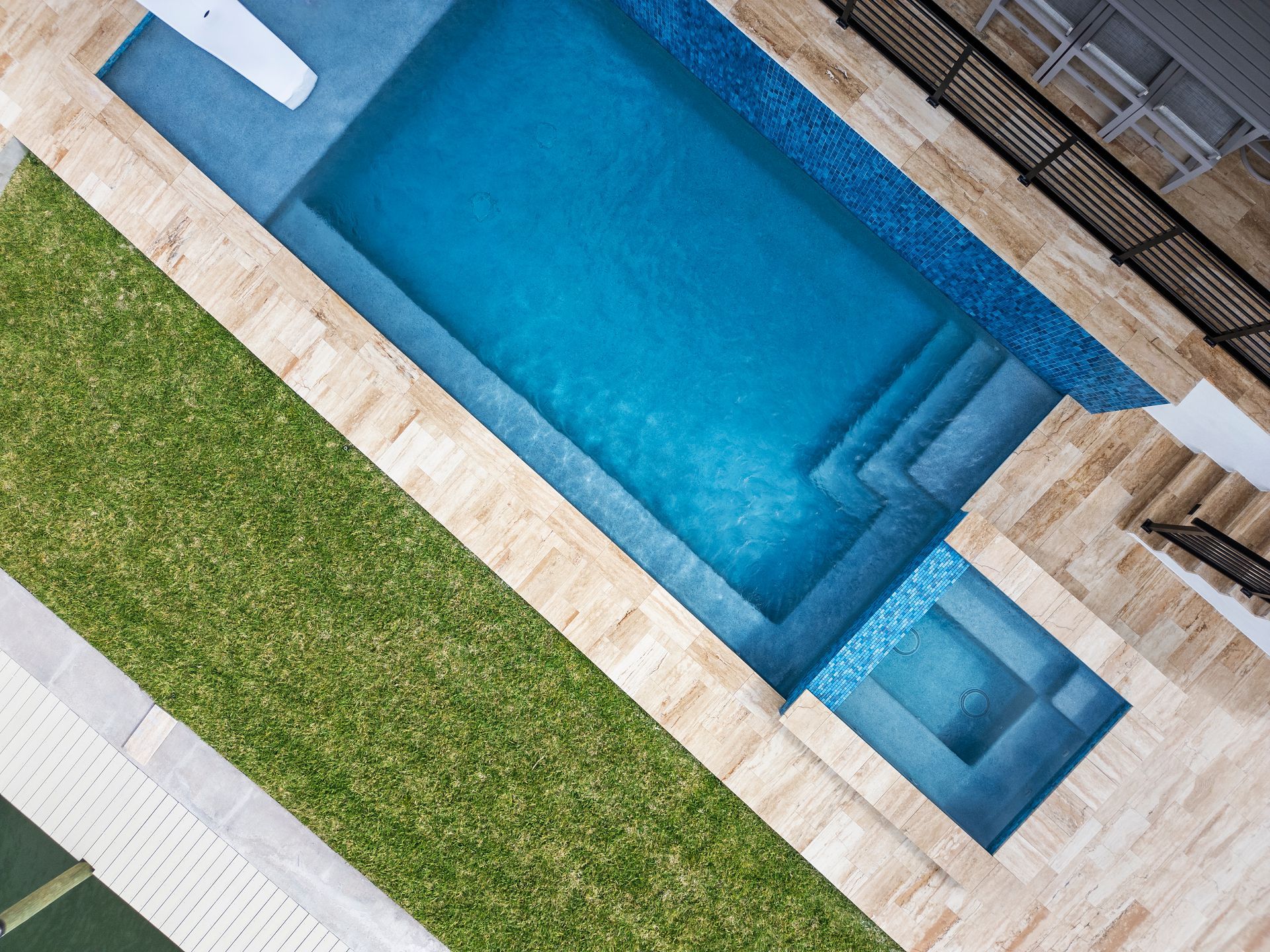 Diagonal view of a turquoise swimming pool beside green lawn and stone patio steps