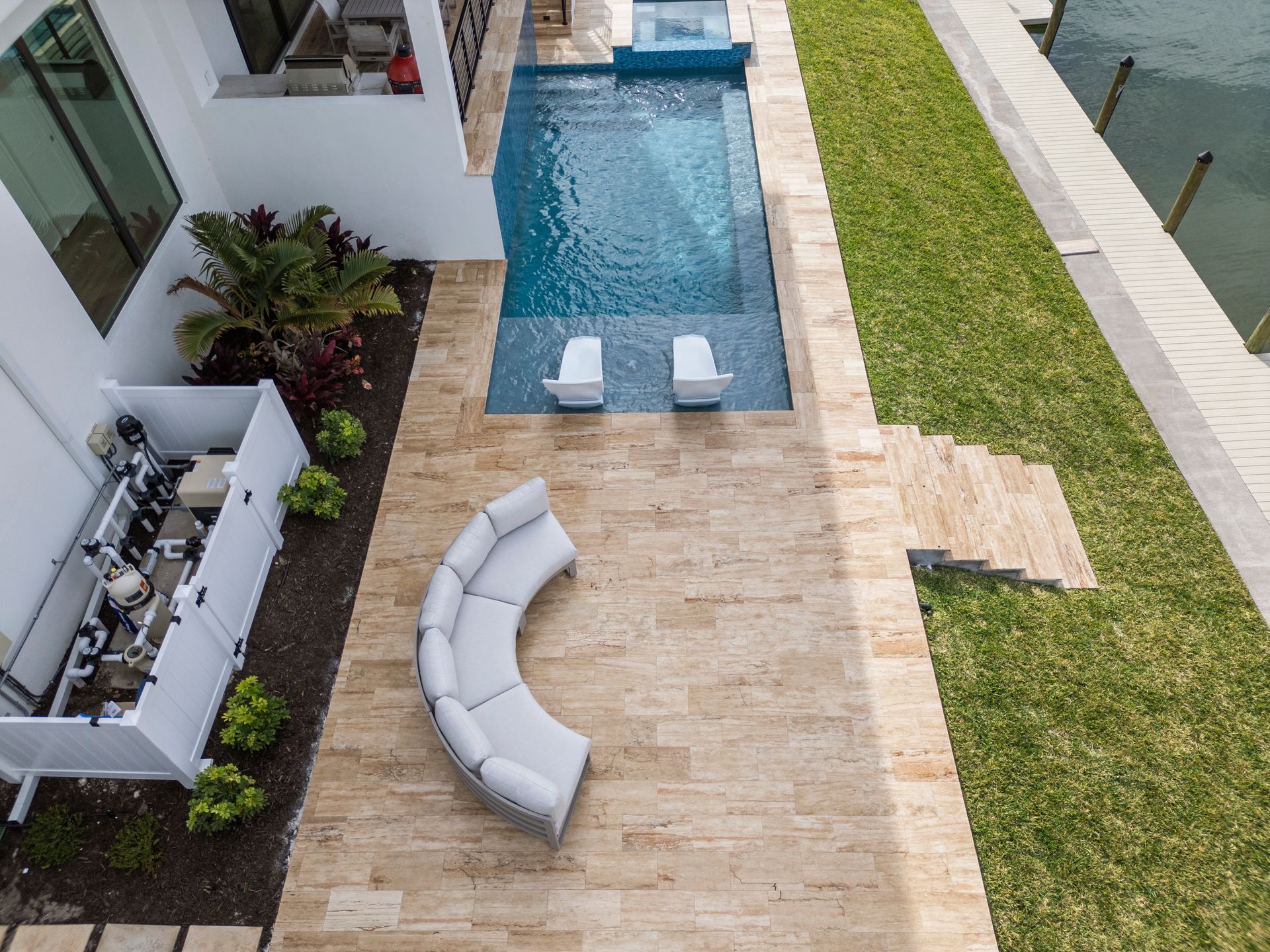 Courtyard pool with white lounge chairs, curved sofa, and grass beside a modern house