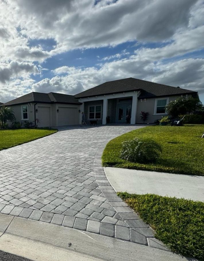 Modern single-story house with a curved paver driveway and green lawn under a cloudy sky