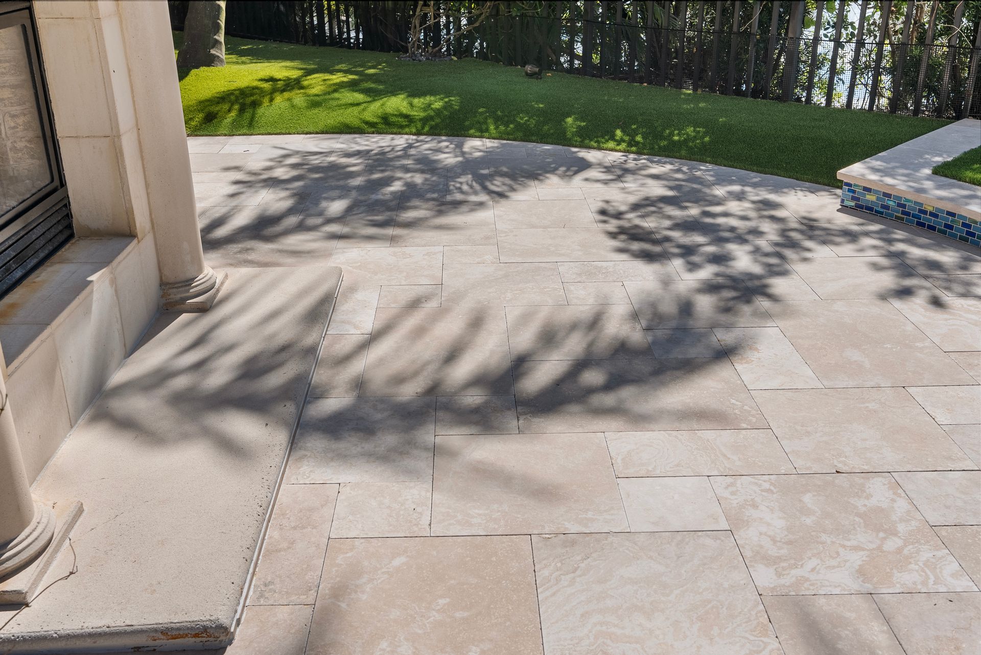 Stone patio beside a building, with tree shadows and a grassy lawn in the background.