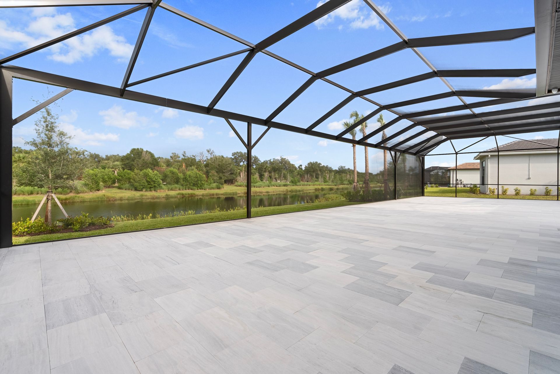 Empty covered patio with light gray floor and open metal frame overlooking a grassy field