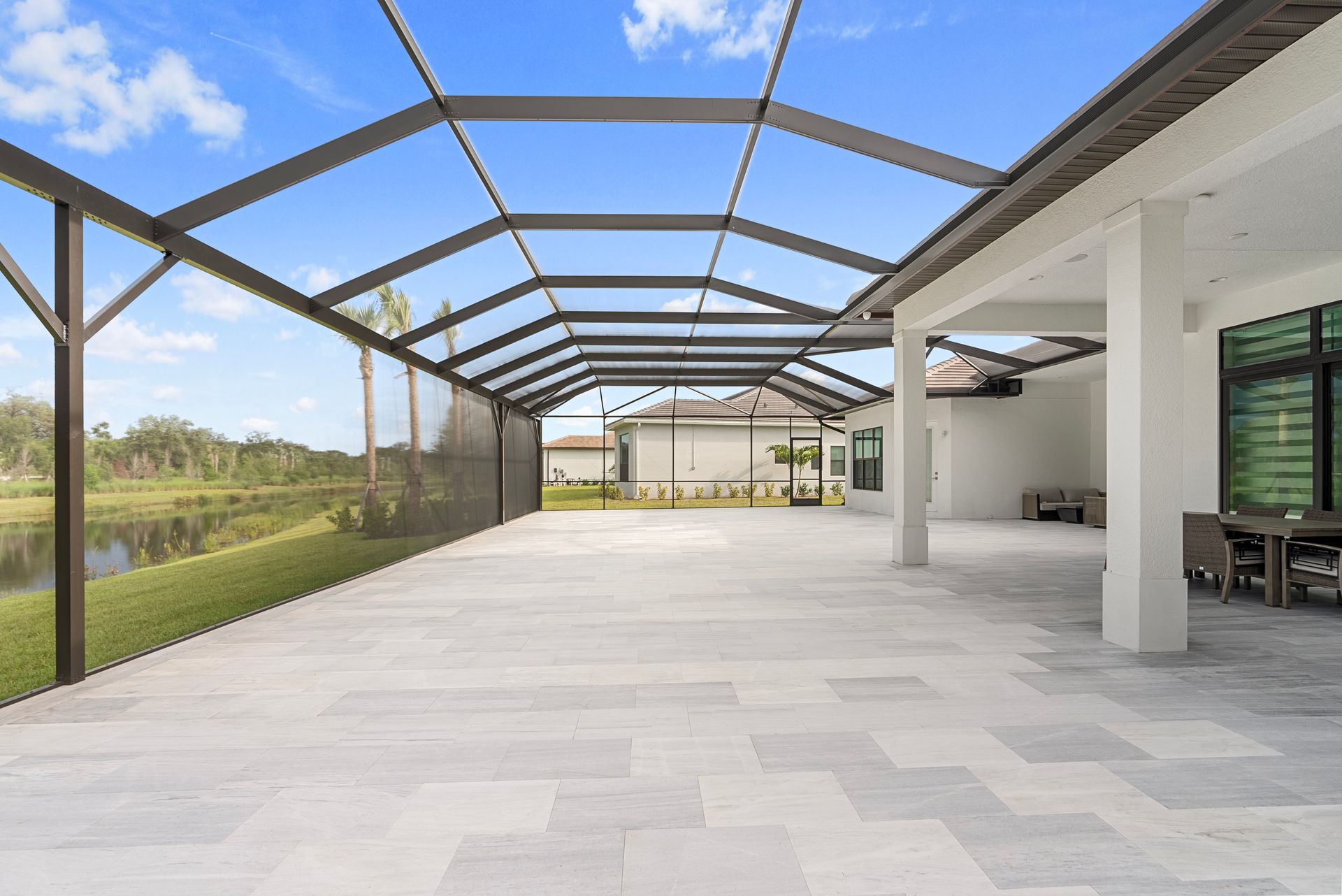 Covered patio with a white tile floor, screened roof frame, and open view of a grassy yard.