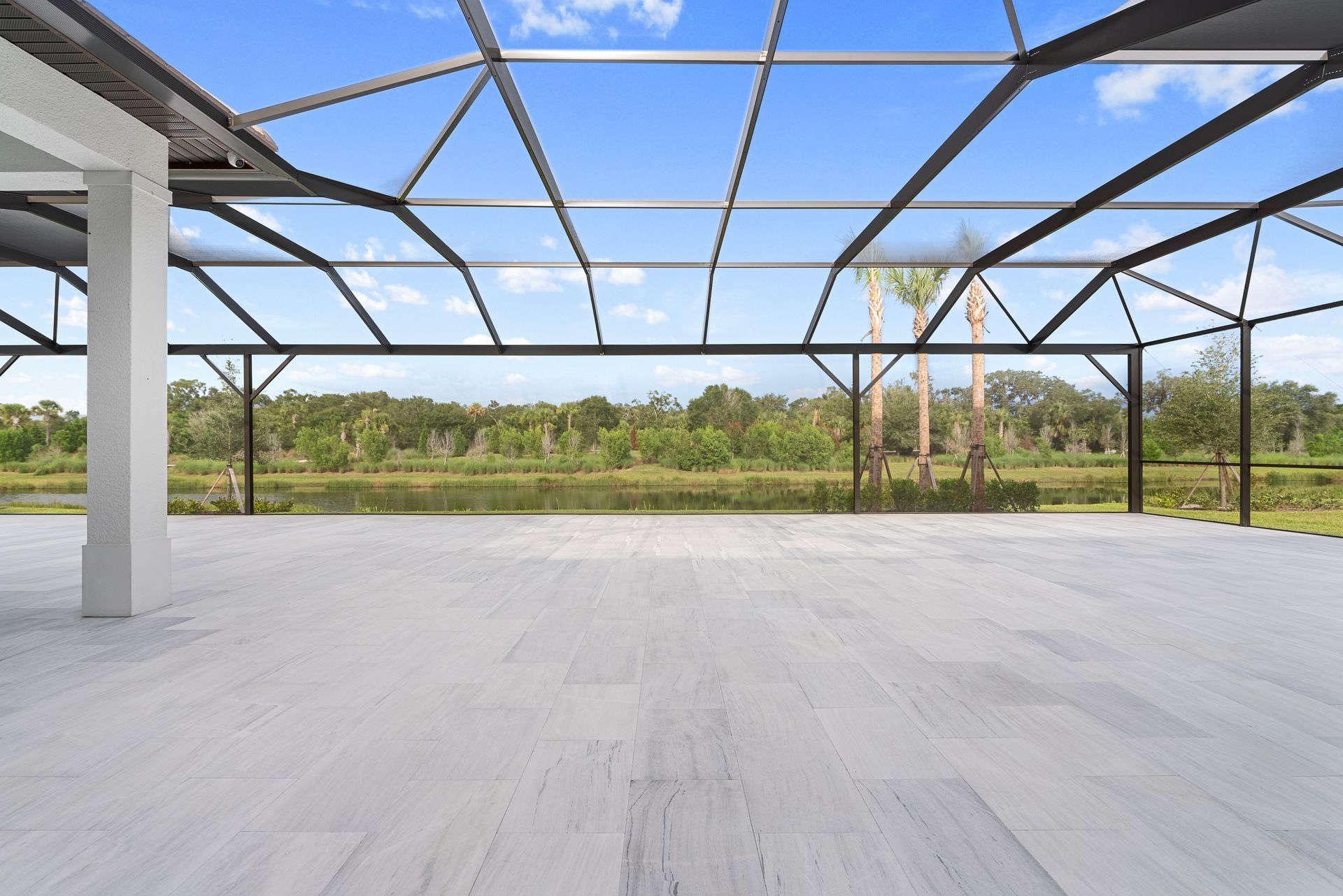 Empty modern pavilion with a steel frame roof, white floor, and green landscape beyond.