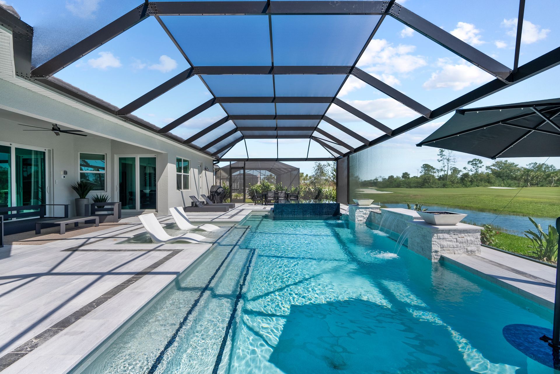 Luxury backyard pool with lounge chairs, covered patio, and water views under a blue screened enclosure