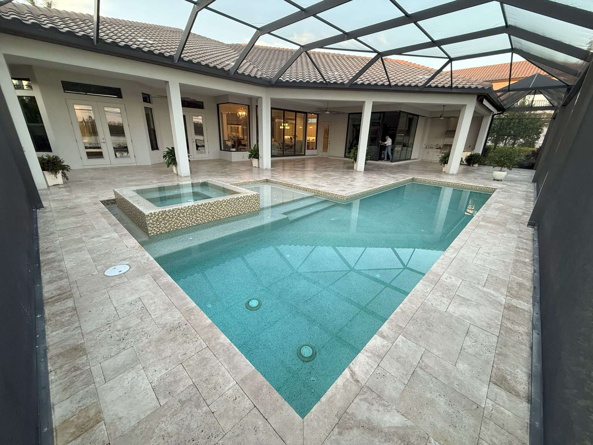Backyard pool courtyard with turquoise water, stone patio, and a covered seating area under a glass roof