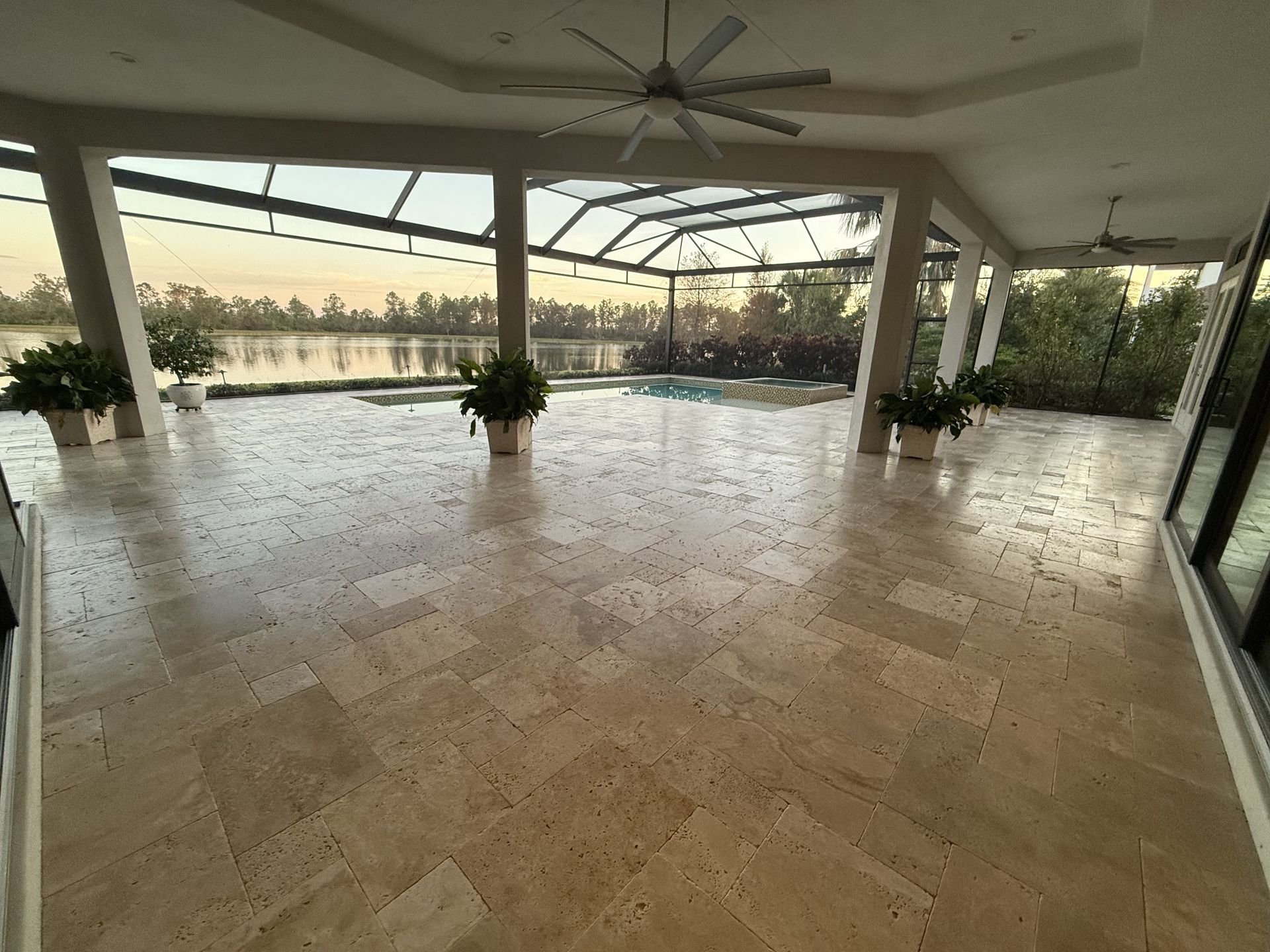 Spacious covered terrace with marble floor, ceiling fans, potted plants, and ocean view at sunset.