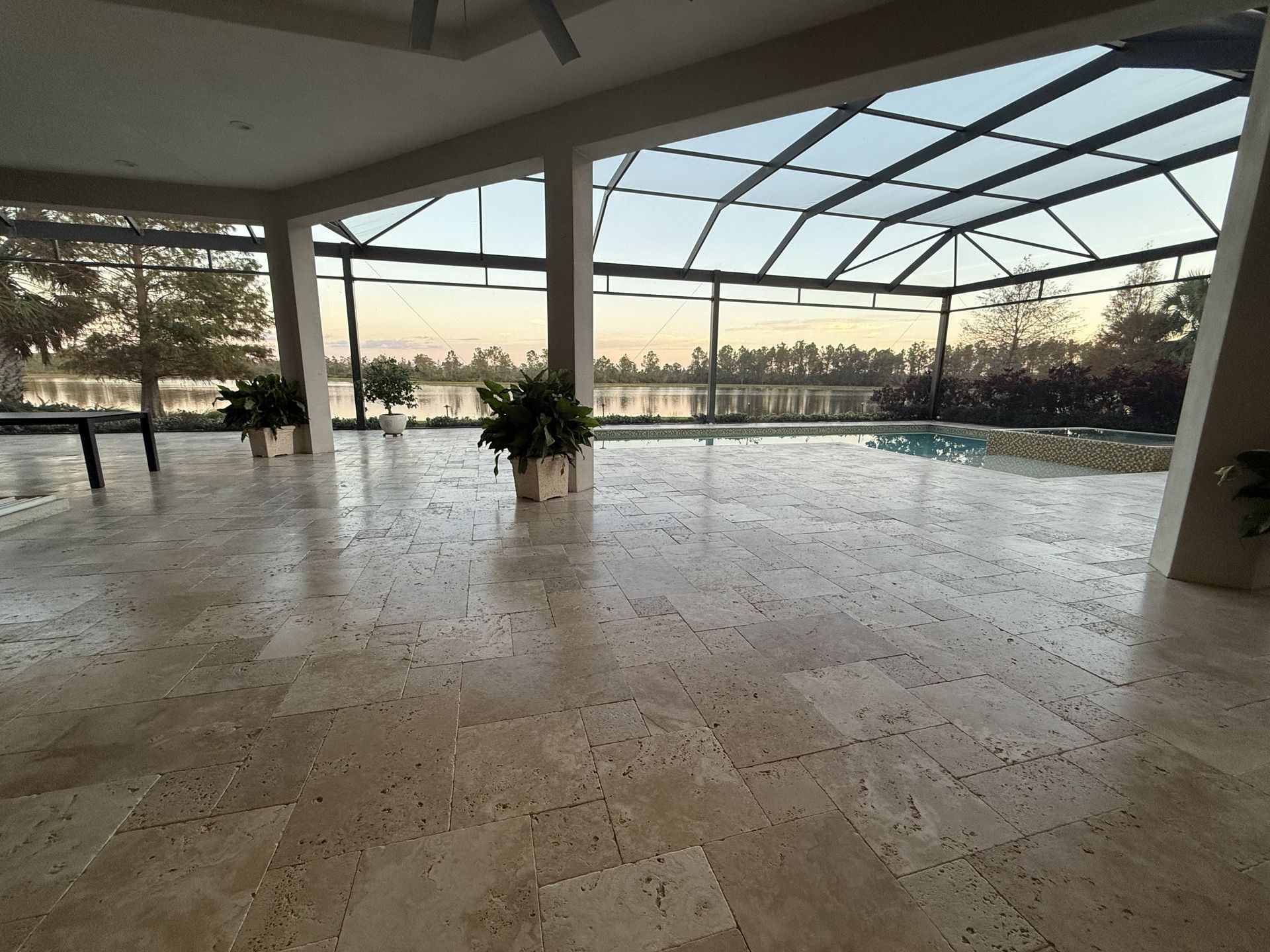 Spacious indoor patio with marble floor, potted plants, and sunset view through glass walls