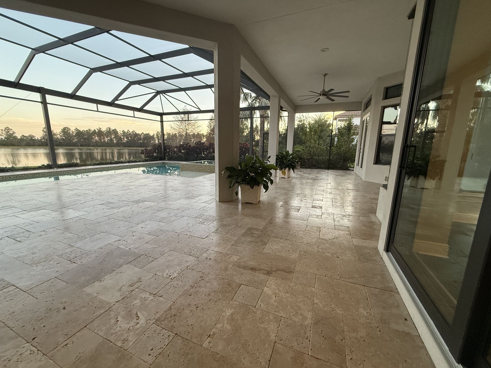 Covered patio with pool, white columns, and sunset view through screened enclosure