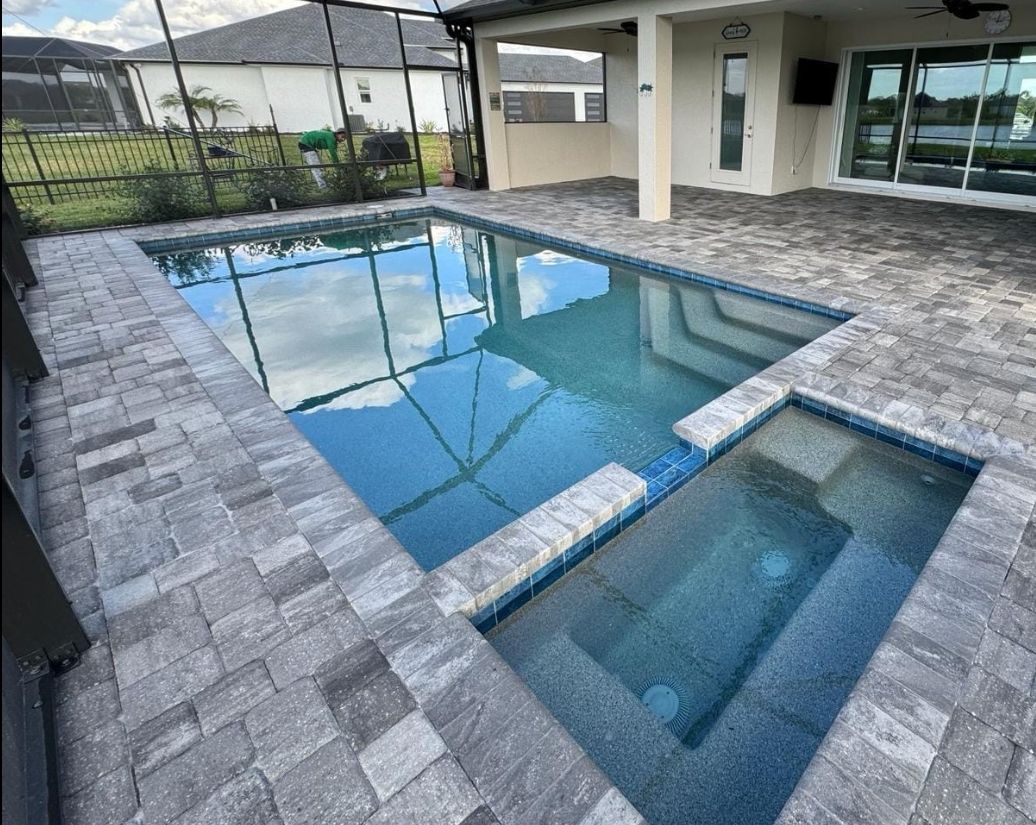 Modern backyard pool with attached hot tub and gray stone patio beside a house