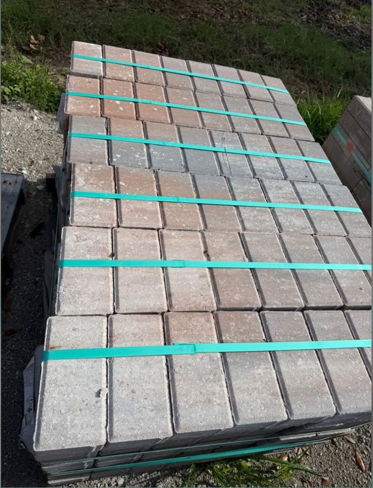 Stacked concrete pavers strapped with teal bands on a pallet outdoors.