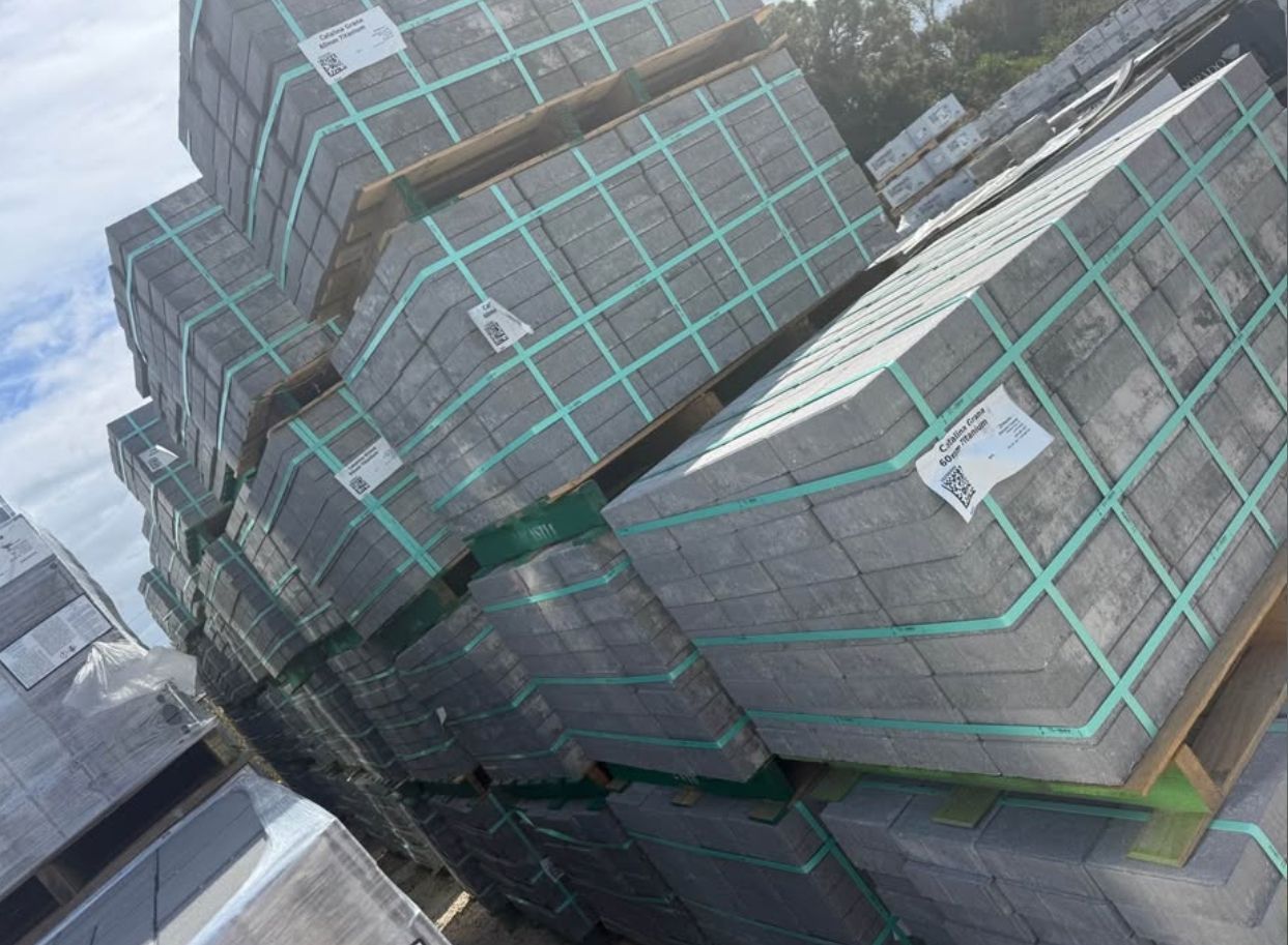 Stacked gray bundled materials secured with green straps on a pallet outdoors