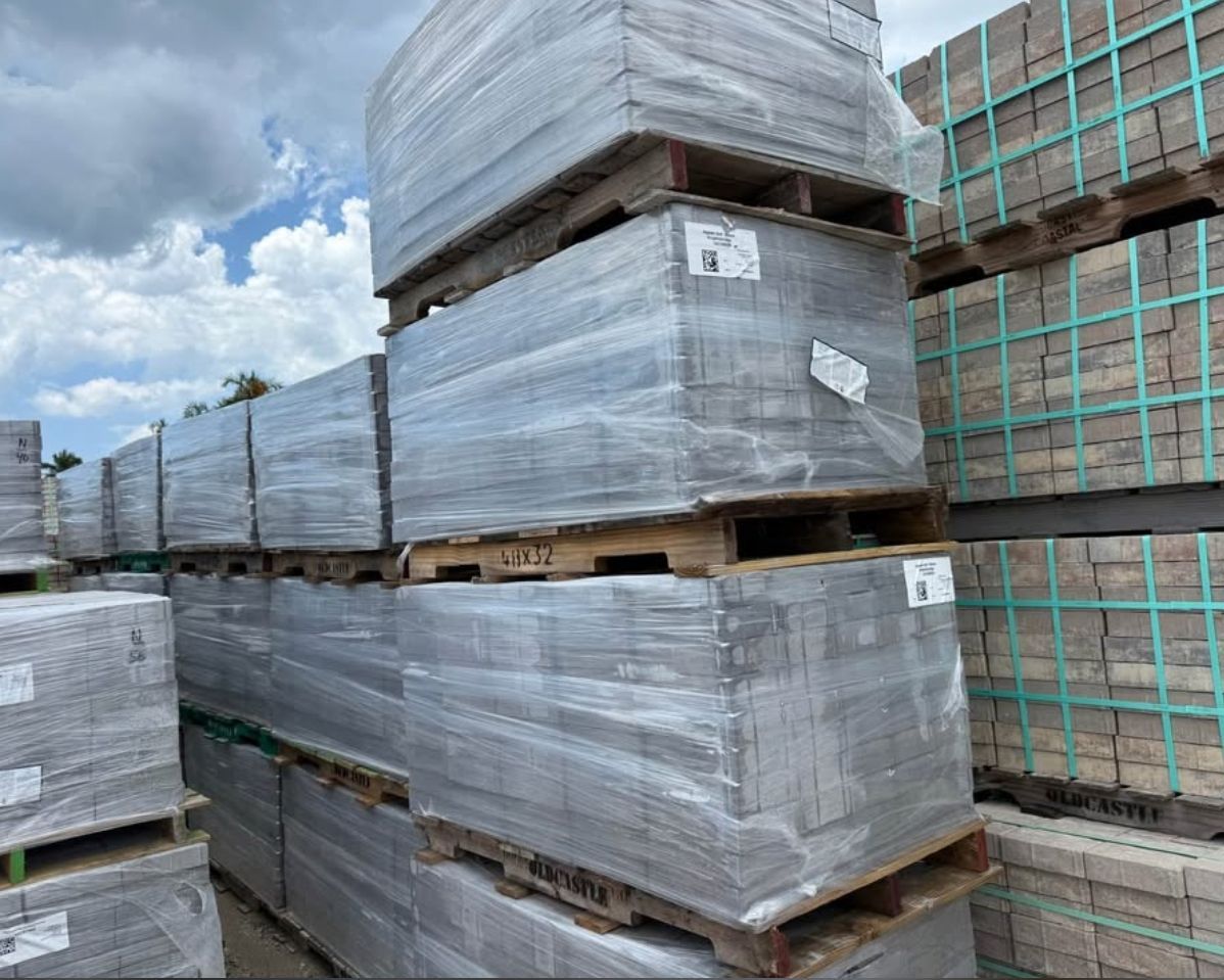 Stacked wrapped pallets of materials in an outdoor storage yard under cloudy sky