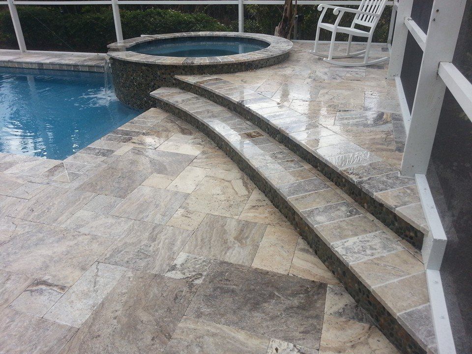 Curved stone steps beside a pool and circular spa on a wet tiled patio