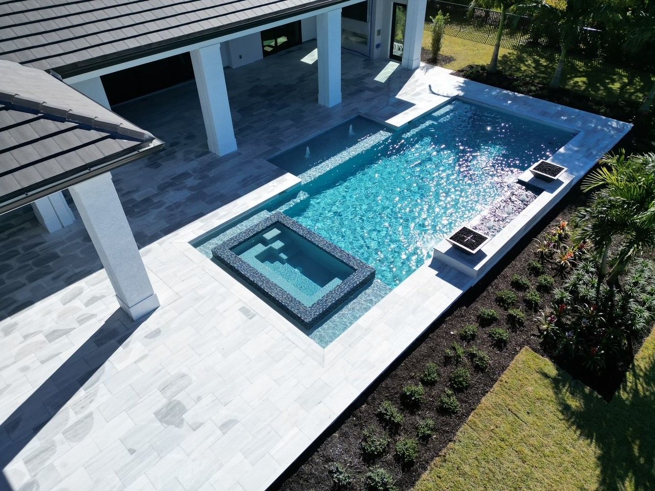 Aerial view of a backyard pool with a raised spa, white patio, and covered seating area.