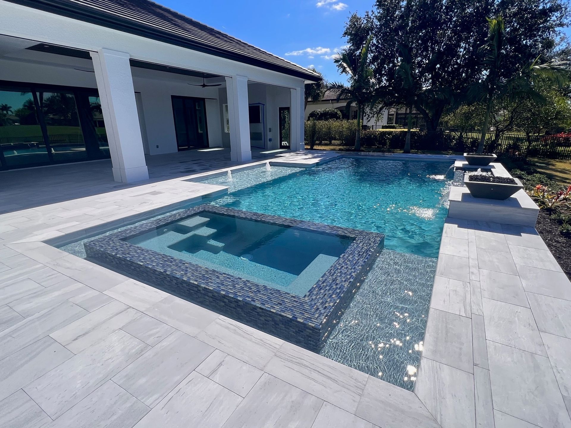 Modern backyard pool with a square spa, white patio, and house exterior in bright sunlight