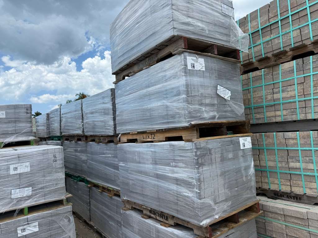 Stacks of shrink-wrapped pallets in a warehouse yard under a cloudy sky