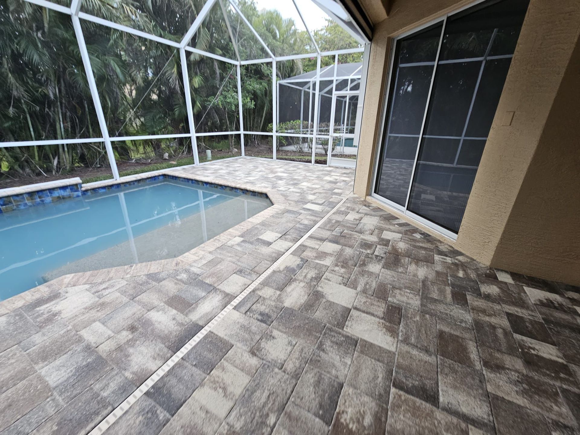 Covered patio with a screened-in pool and gray paver flooring рядом