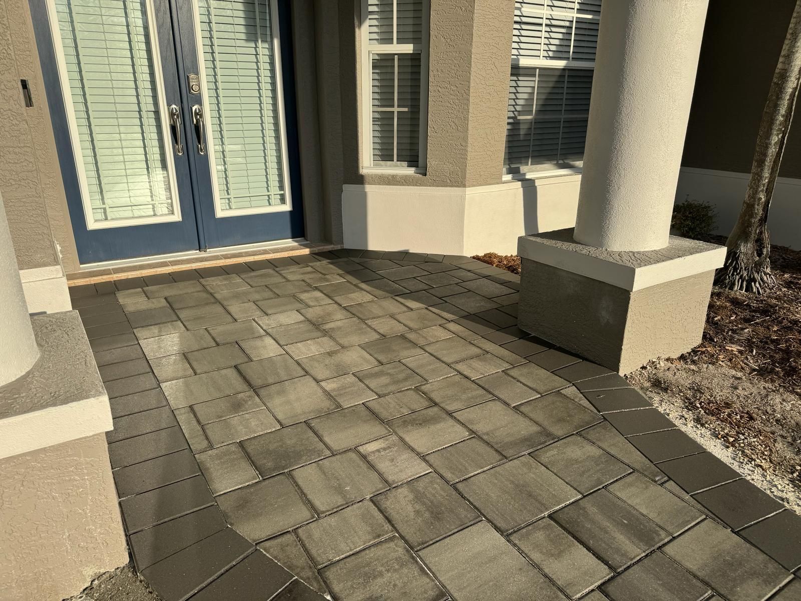 Front porch with blue double doors, stone paver walkway, and white columns by a house entrance