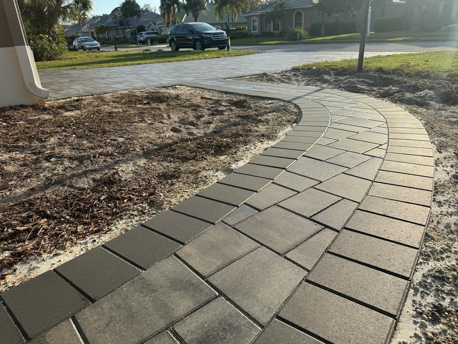 Curved brick walkway beside a mulched yard in a suburban neighborhood