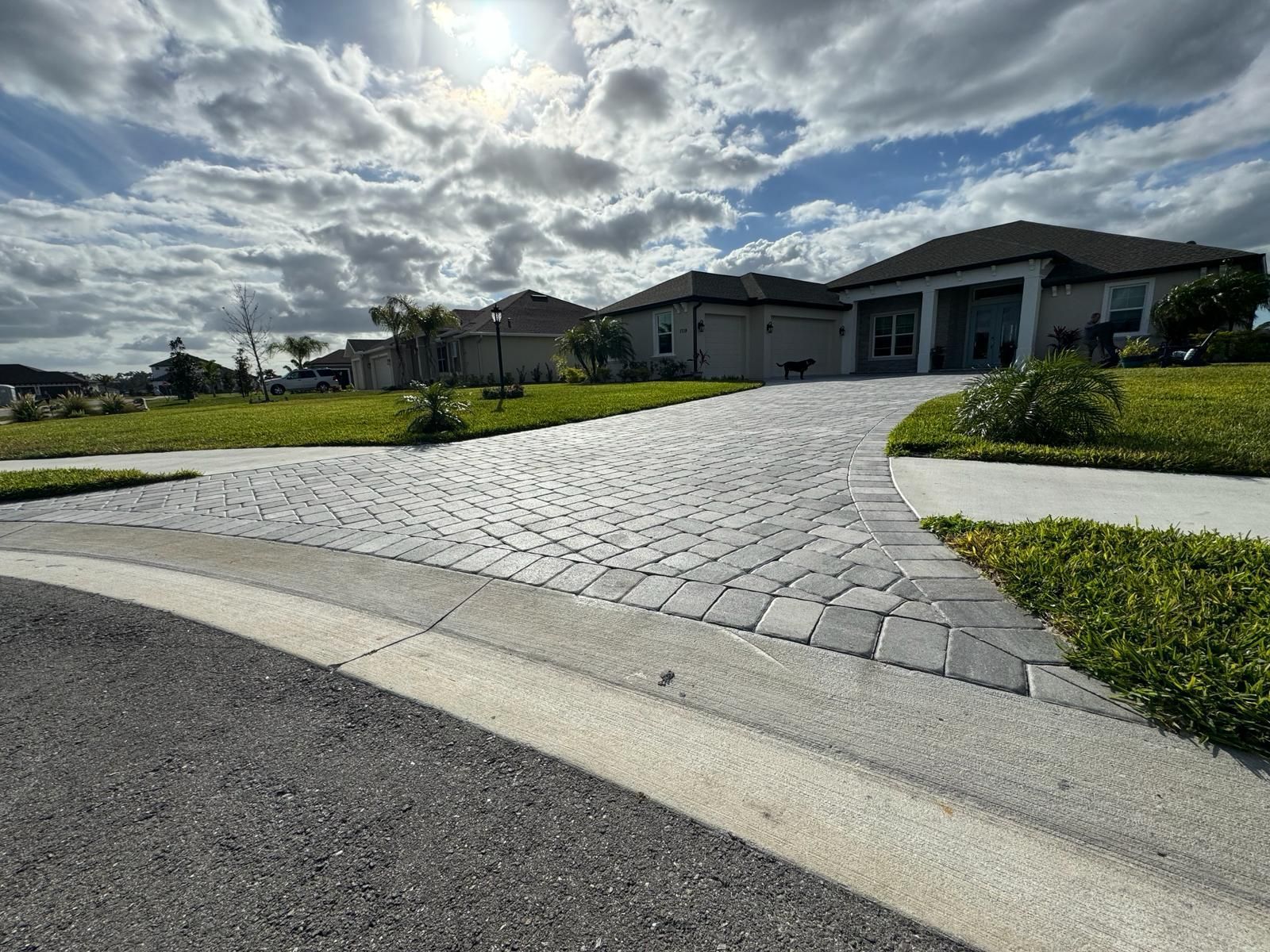 Curved paver driveway leading to a modern house under a bright, cloudy sky