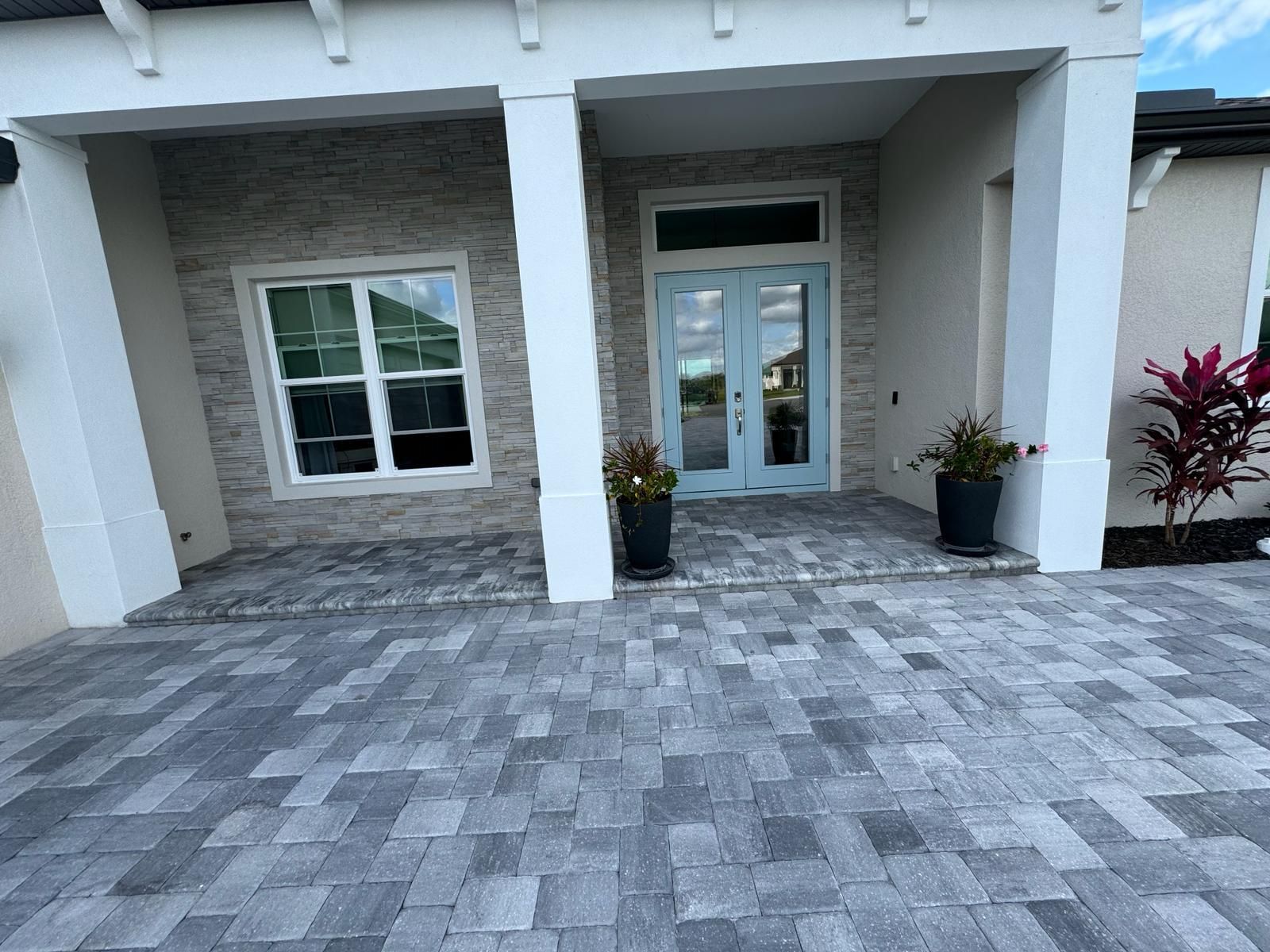 Modern house front entrance with gray paver driveway, white columns, and glass double doors