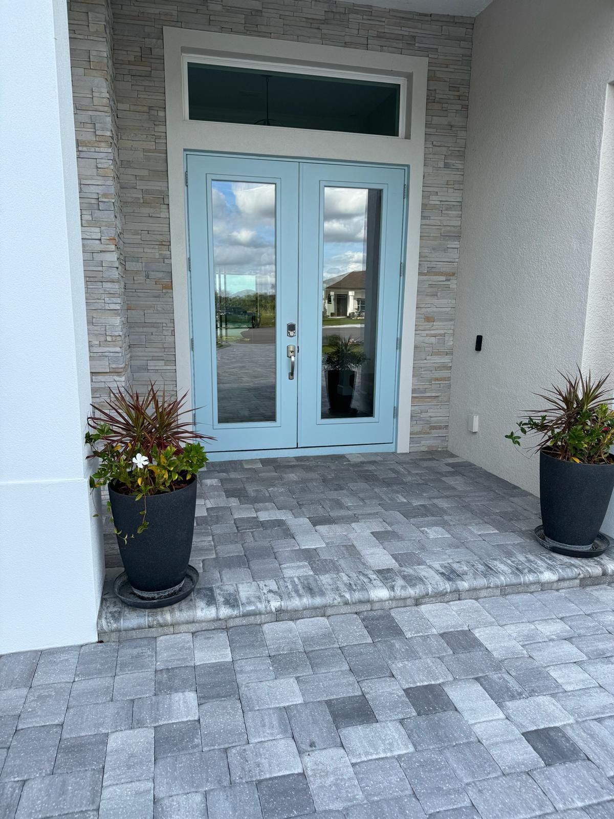 Front entrance with light blue double doors, stone pavers, and two potted plants on either side.