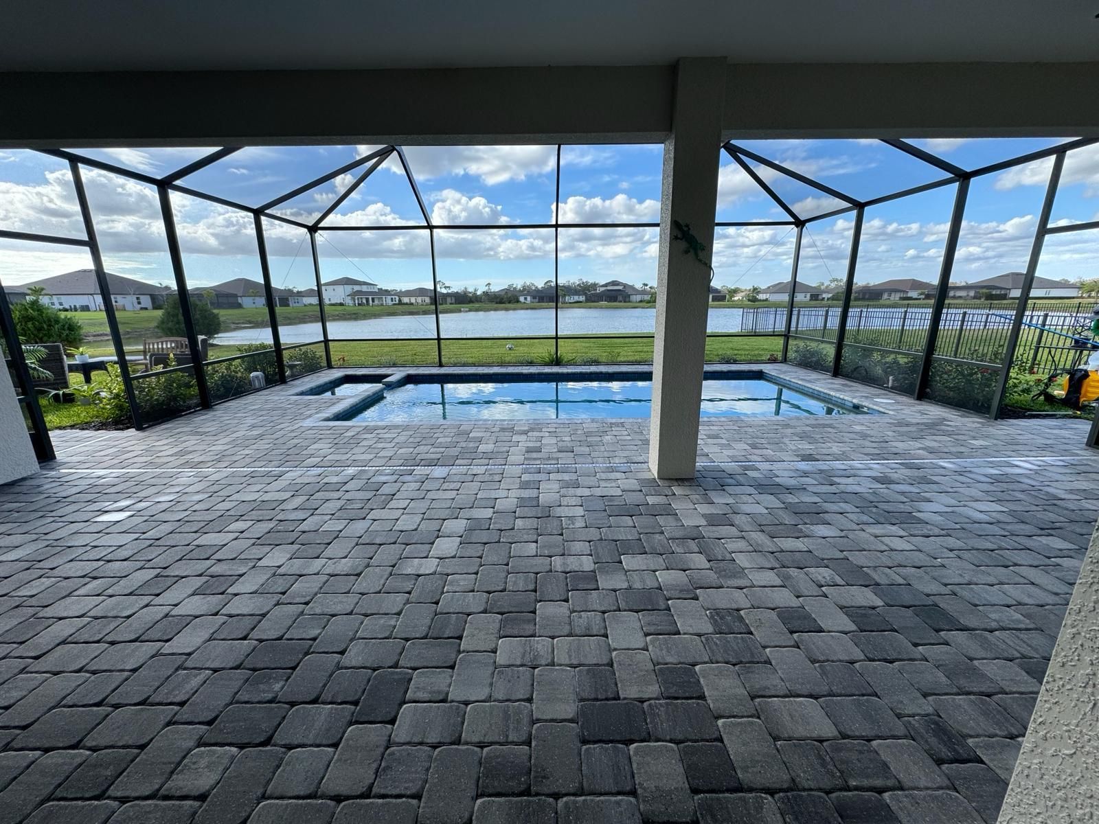 Covered patio with pool, stone paving, and a view of water and greenery beyond