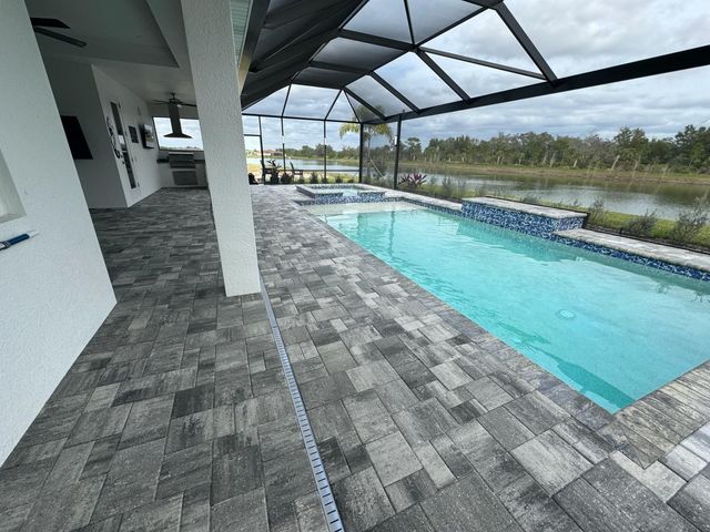 Covered outdoor pool with turquoise water, gray tile deck, and screened patio overlooking greenery